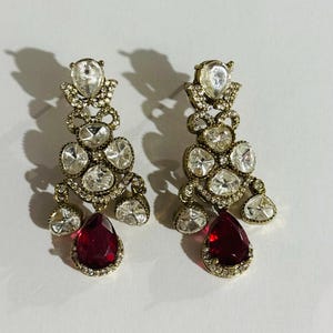 May include: A pair of dangle earrings with a red teardrop-shaped stone and clear rhinestones.
