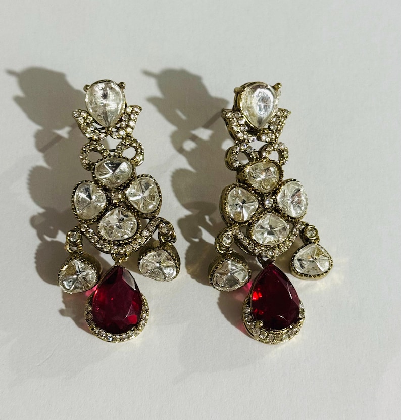 May include: A pair of dangle earrings with a red teardrop-shaped stone and clear rhinestones.