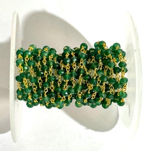 May include: A spool of green gemstone beads strung on a gold chain. The beads are faceted and have a shiny finish.