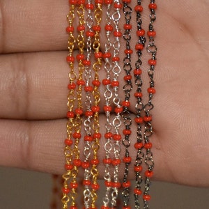 May include: A close-up of six strands of chain with red beads. The chains are made of gold, silver, and black metal.