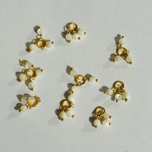 May include: Ten gold-toned metal charms with white pearl-like beads. Each charm has a loop at the top and three beads hanging from it.