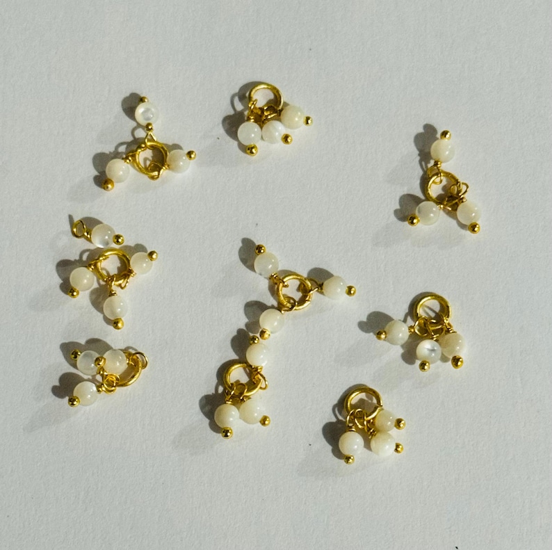 May include: Ten gold-toned metal charms with white pearl-like beads. Each charm has a loop at the top and three beads hanging from it.