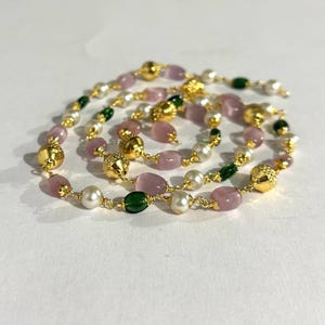 以下が含まれることがあります： スパイラルデザインのゴールドトーンネックレス。ピンク、白、緑のビーズと、テクスチャード加工されたゴールドの球体が特徴です。ビーズは金色のワイヤーで繋がれており、エレガントなアクセサリーです。様々な場面に適しています。