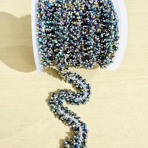 May include: A spool of iridescent black and silver bead chain. The chain is made of small, faceted beads that are strung together with silver wire. The chain is coiled on a white spool.