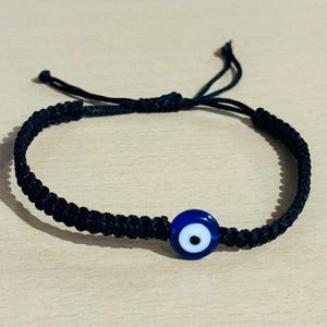 May include: A white ceramic mug with a black handle and the text "But First, Coffee" in a bold, black font. The mug is set against a blurred background, suggesting a cozy setting.