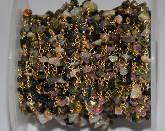 May include: A spool of gemstone chain with small, irregularly shaped tourmaline beads in green, pink, and brown. The beads are strung together with delicate gold-coloured chain links, creating a shimmering, textured effect. Suitable for jewellery making.