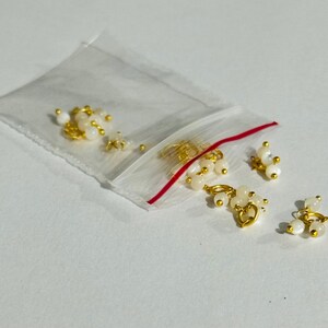 May include: A small plastic bag filled with gold-toned metal charms with white pearl-like beads. The charms are in the shape of a circle with a small loop at the top.