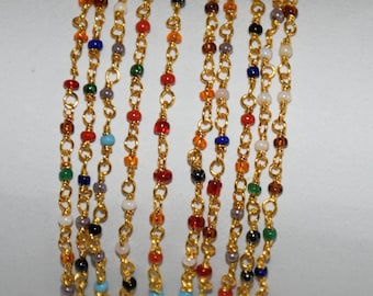 May include: A set of gold chain bracelets with colorful glass beads. The bracelets are layered and feature a variety of colors, including red, blue, green, and white.