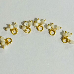 May include: Six gold-toned metal charms with a loop and three white pearl-like beads attached to each loop.