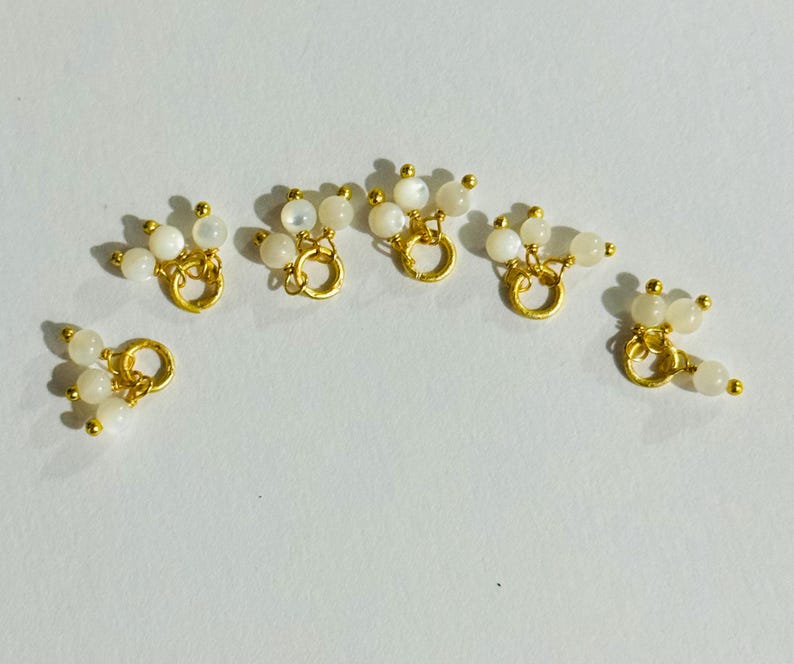 May include: Six gold-toned metal charms with a loop and three white pearl-like beads attached to each loop.