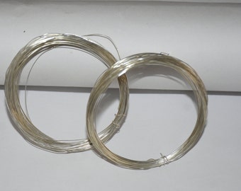 May include: Two spools of silver wire, one on top of the other, on a white surface.