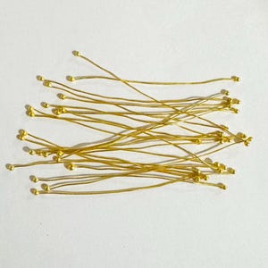 May include: A collection of gold-colored wire floral stems with small round balls at the ends. The stems are arranged in a random pattern on a white surface.