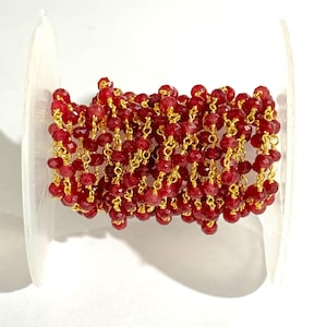 May include: A spool of red gemstone beads with gold chain links. The beads are faceted and the chain is delicate.