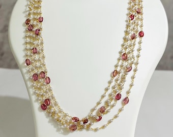 May include: A multi-strand necklace displayed on a white mannequin. The necklace features strands of small white pearls and oval-shaped, translucent, pinkish-purple beads. The beads are interspersed along gold-colored chains, creating a layered effect.