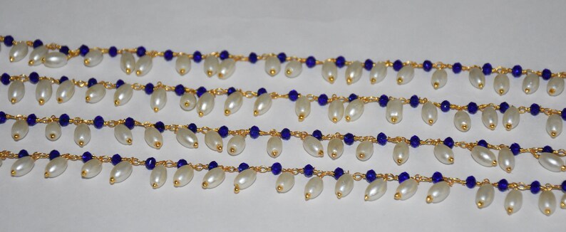 K&ouml;nnte beinhalten: Eine Str&auml;hne aus wei&szlig;en Perlen mit dazwischenliegenden blauen Glasperlen, auf einer goldenen Kette aufgef&auml;delt. Die Perlen sind in einem kaskadierenden Muster angeordnet, was einen zarten und eleganten Look erzeugt.