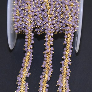 Puede incluir: Un carrete de cadena dorada con cuentas de vidrio lavanda. La cadena está hecha de pequeñas piezas de metal unidas y las cuentas son facetadas y tienen un ligero brillo.