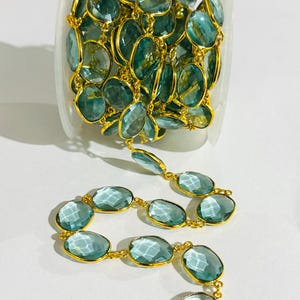 Puede incluir: Un rollo de cadena de piedras preciosas azul claro con conectores de metal dorado. La cadena está hecha de piedras preciosas de forma ovalada y es perfecta para la elaboración de joyas.