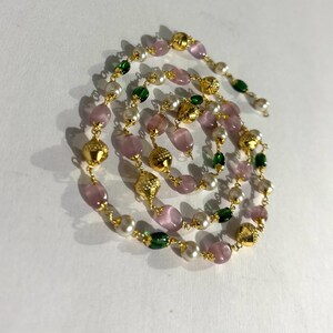以下が含まれることがあります： スパイラルデザインの繊細なネックレス。ピンク、グリーン、ホワイトのビーズと、ゴールドカラーのテクスチャードビーズが交互に配置されています。ビーズはゴールドカラーのチェーンで繋がれています。
