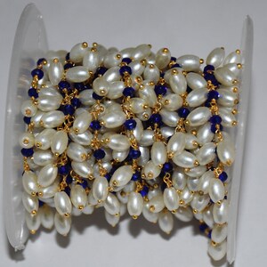 K&ouml;nnte beinhalten: Eine Spule mit einer Kette aus wei&szlig;en Perlen und blauen Glasperlen. Die Kette ist aus goldfarbenem Metall und perfekt f&uuml;r die Schmuckherstellung.