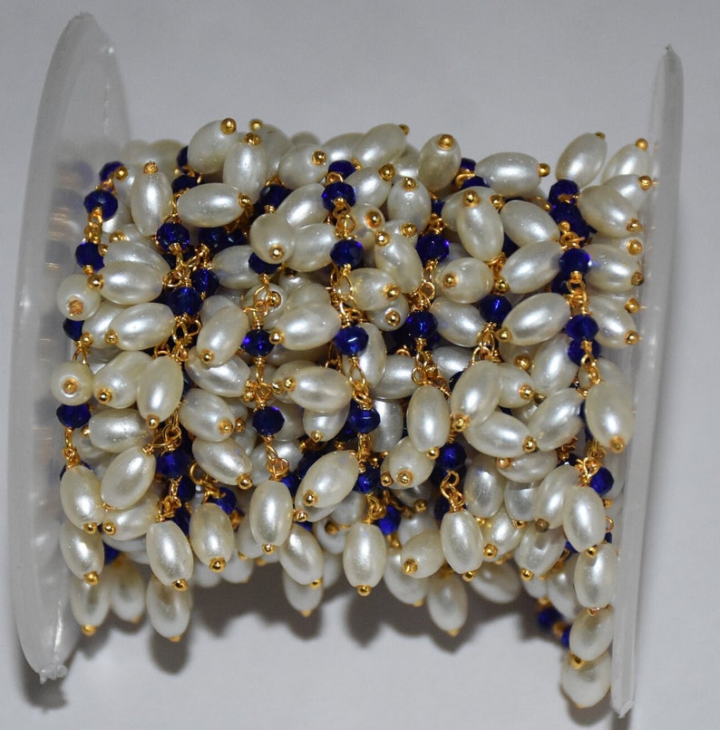 K&ouml;nnte beinhalten: Eine Spule mit einer Kette aus wei&szlig;en Perlen und blauen Glasperlen. Die Kette ist aus goldfarbenem Metall und perfekt f&uuml;r die Schmuckherstellung.