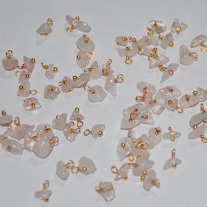 May include: A collection of small, irregular, white gemstone charms with gold jump rings and beads. The charms are scattered on a white surface.