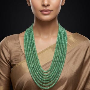 Peut inclure: Un collier à plusieurs rangs composé de petites perles rondes vert clair. Le collier est drapé autour du cou et de la poitrine. Le modèle porte un chemisier de couleur beige.