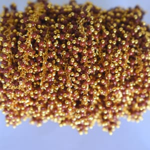May include: A close-up of a gold chain with brown beads. The chain is coiled up and the beads are visible throughout the image.
