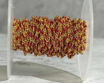 May include: A spool of gold chain with red beads. The chain is wrapped around a clear plastic spool.