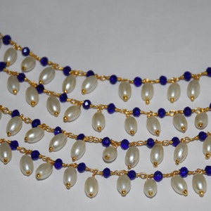 K&ouml;nnte beinhalten: Eine mehrreihige Halskette mit wei&szlig;en ovalen Perlen und blauen Glasperlen an einer goldenen Kette.