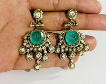 Può includere: Un paio di orecchini dorati ornati con grandi pietre verde smeraldo a taglio quadrato. Gli orecchini sono adornati con pietre preziose più piccole e trasparenti e dettagli di filigrana intricati.