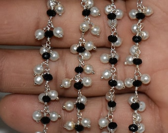 Op de afbeelding: Een zilveren ketting met zwarte en witte kralen. De ketting heeft een delicaat ontwerp met kleine, ronde kralen.