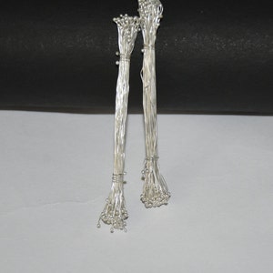 Puede incluir: Dos paquetes de alambre floral plateado con pequeñas cuentas plateadas en los extremos. El alambre está agrupado y atado con alambre plateado.