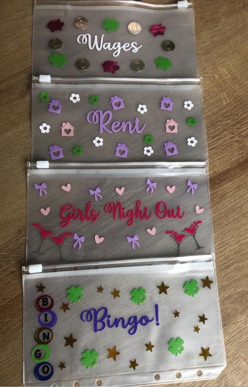 May include: Four translucent plastic zipper pouches with white zippers. The first pouch features the word Wages with piggy bank and coin icons. The second says Rent with house and flower icons. The third says Girls Night Out with martini glasses and bows. The fourth says Bingo! with bingo balls and stars.