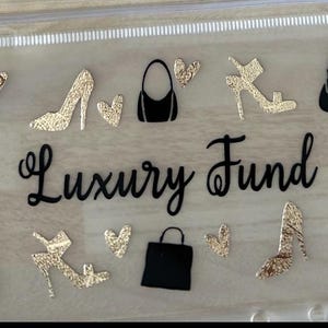 May include: A clear plastic zip-up pouch featuring the black script text Luxury Fund in the centre. The pouch is decorated with black and gold glitter silhouettes of various handbags, high-heeled shoes, and small heart shapes scattered across the surface.