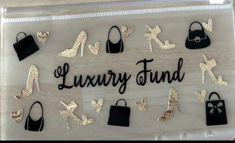 May include: A clear plastic zip-up pouch featuring the black script text Luxury Fund in the centre. The pouch is decorated with black and gold glitter silhouettes of various handbags, high-heeled shoes, and small heart shapes scattered across the surface.