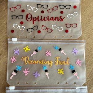 May include: Four translucent, rectangular zipper pouches with six holes along the bottom edge. The top pouch features toothbrushes, stars, a tooth, and the word Dentist. The second has glasses and the word Opticians. The third has paintbrushes, splatters, and Decorating Fund. The fourth has chairs, hearts, and Furniture.