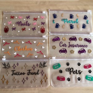 May include: Six translucent plastic zipper pouches with six-hole punched edges. Each pouch features unique vinyl decals and text: Nails with bows and polish bottles, Petrol with gas pumps and pound signs, Clothes with hangers and hearts, Car Insurance with cars and flowers, Tattoo Fund with swallows and stars, and Pets with bowls and paw prints.