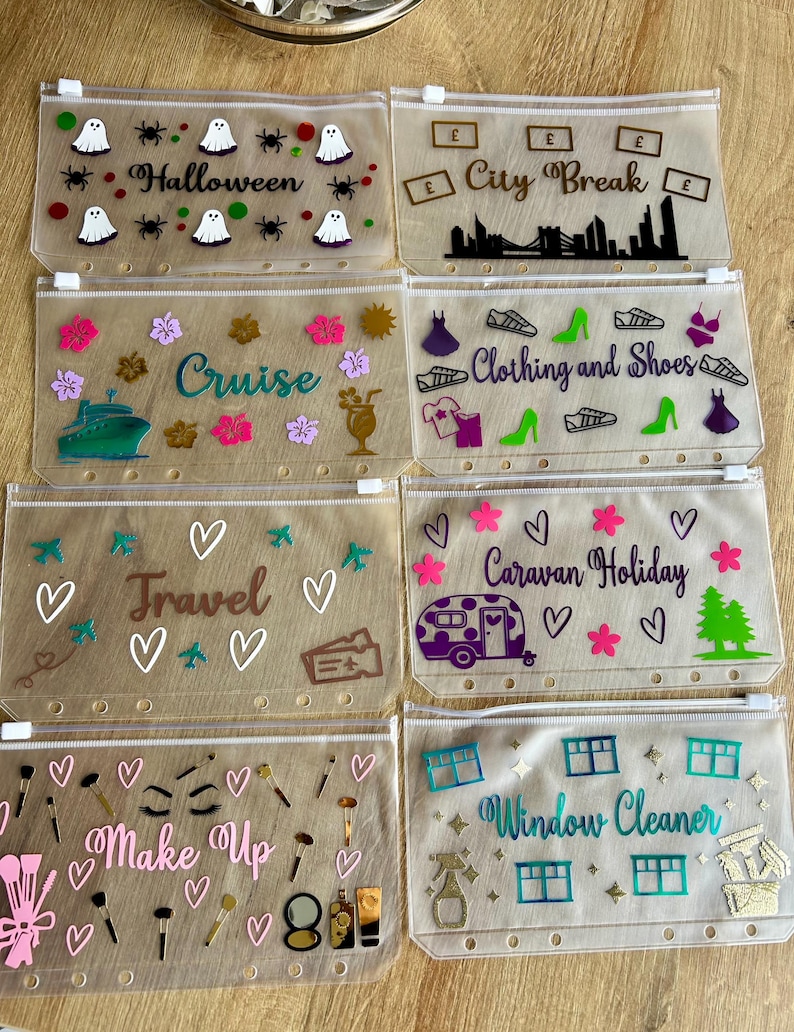 May include: Eight translucent plastic zipper pouches with punched holes for binders. Each pouch features unique vinyl decals including text like Halloween, City Break, Cruise, Clothing and Shoes, Travel, Caravan Holiday, Make Up, and Window Cleaner.