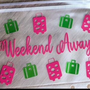 May include: A clear plastic zip-up pouch featuring the hot pink text "Weekend Away" in a cursive font, surrounded by a repeating pattern of hot pink and bright green suitcase icons with various circular and star-shaped cutouts on the luggage.