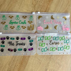 May include: Four rectangular, translucent plastic zipper pouches with white zippers and punched holes for binders. Each pouch features unique vinyl decals: green money bags and gold coins labelled Spare Cash, food items labelled Lunch Dates, paw prints and bowls labelled Pet Treats, and green euro bills labelled Euros.