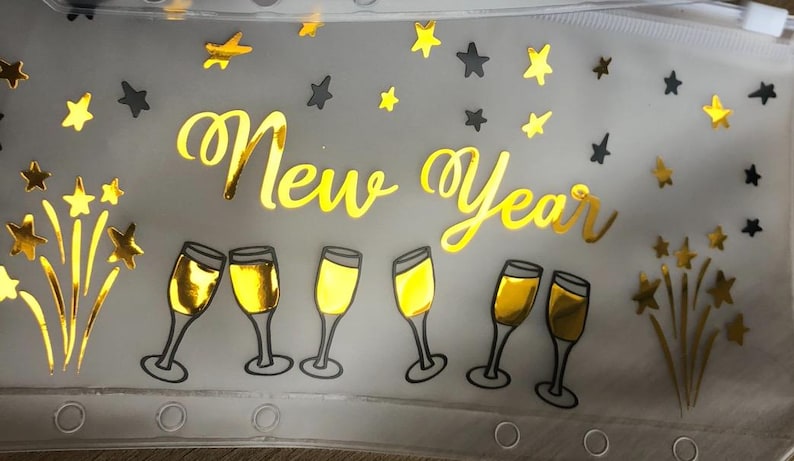 May include: A translucent zippered pouch featuring the gold foil text New Year. The design includes gold foil illustrations of six champagne flutes and various star shapes scattered across the surface. The pouch has a row of circular holes along the bottom edge.