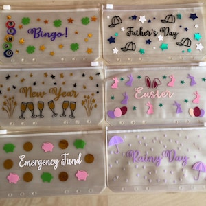 May include: Six translucent plastic zip-lock pouches with white plastic sliders and six holes along the bottom edge. Each pouch features unique vinyl decals: Bingo with BINGO letters, Father's Day with hats, New Year with champagne glasses, Easter with bunnies and eggs, Emergency Fund with coins and pigs, and Rainy Day with umbrellas and raindrops.