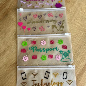 May include: Four translucent plastic zipper pouches with white zippers and punched holes for binders. The top pouch features the text Annual Savings with months and pound symbols. The second shows Anniversary with hearts and champagne. The third says Passport with suitcases and flowers. The bottom displays Technology with icons of phones, laptops, and Wi-Fi symbols.