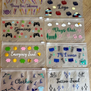 May include: Eight clear plastic zipper pouches for binders, each featuring unique labels and colourful vinyl decals. Labels include Dining Out/Takeaway, Lego, Gaming, Days Out, Emergency Fund, TV License, Clothes, and Tattoo Fund with matching icons.