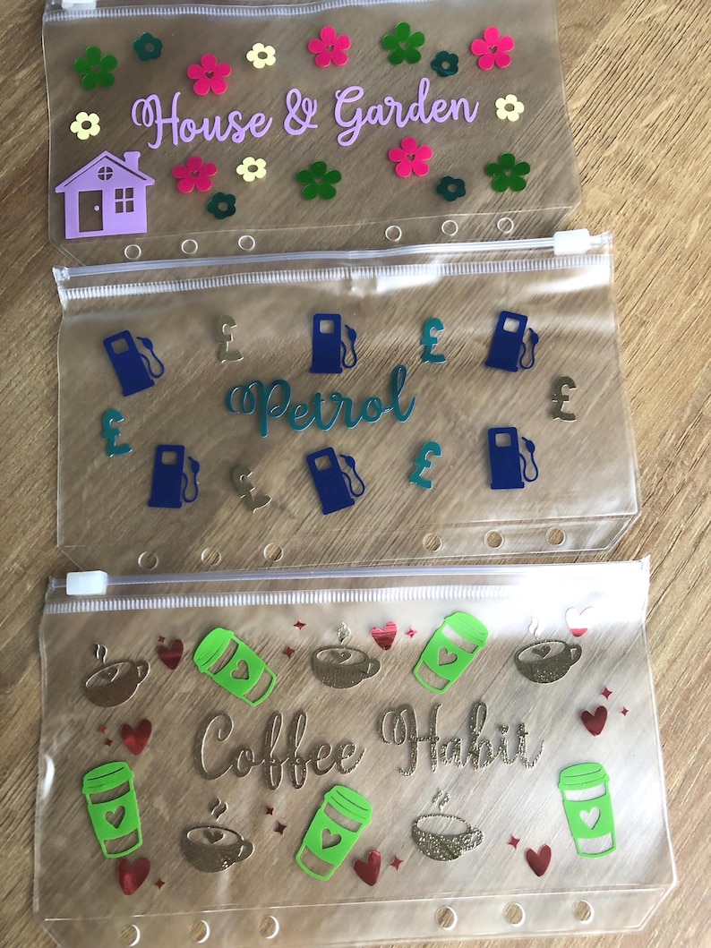 May include: Three translucent plastic zipper pouches with six-hole punched edges. The top pouch features a purple house, flowers, and the text House & Garden. The middle pouch shows blue gas pumps and pound symbols with the text Petrol. The bottom pouch displays green coffee cups, brown coffee mugs, and the text Coffee Habit.