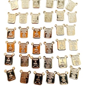 May include: Mini scapular charms in gold tone, featuring religious text and symbols. The charms are rectangular with rounded tops and small loops for attachment. The image includes text: "DEUS E FIEL" and "Mini Scapular Charms".