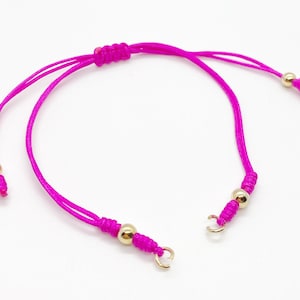 May include: A pink string bracelet with gold beads and clasps. The bracelet is adjustable and can be worn on the wrist or ankle.