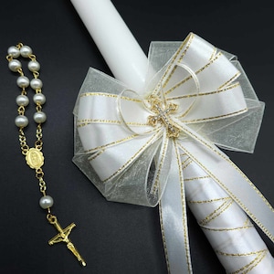 May include: A white candle with a gold and white ribbon bow and a small gold cross with rhinestones. A white pearl rosary with a gold cross and a gold pendant with a religious image is also included.