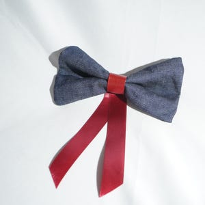 Può includere: Un papillon in denim blu scuro con una fascia in pelle rossa e code di nastro rosse abbinate. Il papillon è su uno sfondo bianco. Questo accessorio è adatto per eventi formali. Circa 10 cm di larghezza.
