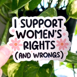 May include: White sticker with black text that reads "I support women's rights (and wrongs)". The sticker is decorated with pink flowers.